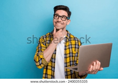 Portrait of smart guy with stubble wear checkered shirt in glasses holding laptop look empty space offer isolated on blue color background