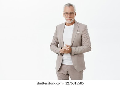 Portrait of smart and handsome intelligent senior male professor in stylish suit and glasses holding hands together against chest and gazing with self-assured wise expression at camera giving speech