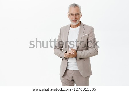 Portrait of smart and handsome intelligent senior male professor in stylish suit and glasses holding hands together against chest and gazing with self-assured wise expression at camera giving speech