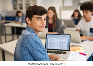 Portrait Of Smart High School Guy In Looking At Camera. Close Up Face Of Proud College Student Studying In Classroom. Smiling University Guy Looking Behind While Studying On Laptop In University.