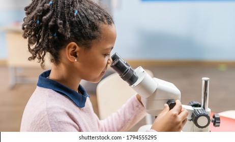 Portrait Of Smart Little Schoolgirl Looking Under The Microscope. In Elementary School Classroom Cute Girl Uses Microscope. STEM (science, Technology, Engineering And Mathematics) Education Program