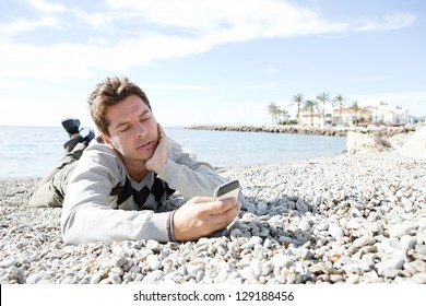 Portrait Of A Smart Man Laying Down On The Shore Of A White Pebble Beach Being Thoughtful While Using A 