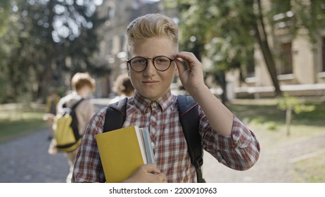 Portrait Of Smart School Boy Adjusting Eyeglasses And Holding Books, Getting Proper Education