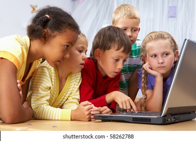 Portrait of smart schoolgirls and schoolboys looking at the laptop