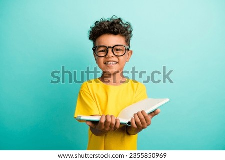 Portrait of smart small boy with brown hair wear stylish t-shirt in glasses hold book do homework isolated on teal color background