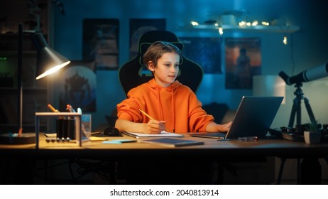 Portrait Of A Smart Young Boy Doing Homework On A Laptop Computer In Cozy Dark Room At Home. Teenager Is Concentrated And Doing Math. Home Education Concept.