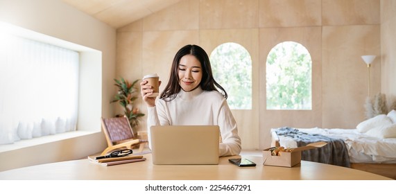 Portrait of sme business asian woman work from home at online computer desktop table hand hold coffee cup. Asia freelancer girl use laptop in bed room. Small business sme digital network, technology. - Powered by Shutterstock