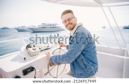 Portrait smile happy man driver captain of white luxury yacht holding helm wheel, summer travel on boat sea.