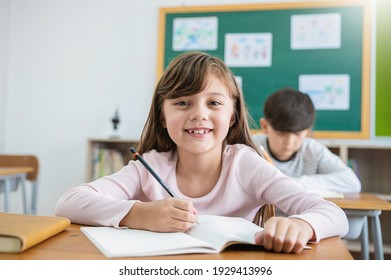 Portrait of smile little caucasian pupil writing at desk in classroom at the elementary school. Student girl doing test in primary school. Education knowledge children writing notes in classroom. 