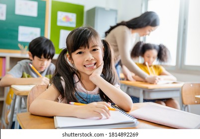 Portrait of smile little pupil writing at desk in classroom at the elementary school. Student girl doing test in primary school. Children writing notes in classroom. Education knowledge concept