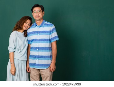 Portrait of a smiley happy loving Asian couple dressed casually standing relaxedly, smiling to a camera for studio shot over green background. Warmth family concept.