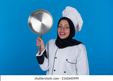 Portrait of smiley veiled female chef wearing the uniform holds silver pan raising it showing on blue background. - Powered by Shutterstock