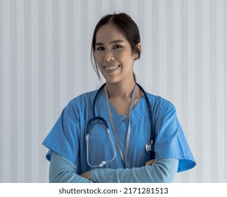 Portrait Of Smiley Young Asian Female Doctor In Blue Gown Standing With Arm Crossed Looking At Camera, Happy Woman Doctor Wearing Stethoscope In Hospital, Health And Medical Concept 