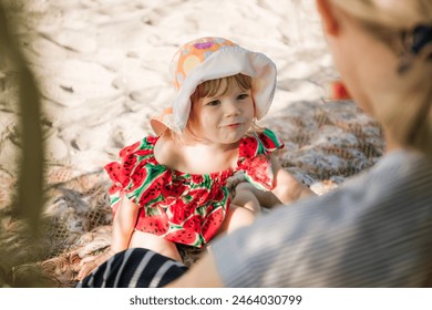 Portrait of smiling 2 year old child speaking with mother. Mom and daughter. Little girl sits on the beach in dress with watermelon print. Family summer time rest. Close-up. Copy space. Happy moments. - Powered by Shutterstock