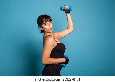 Portrait of smiling active trainer showing arm muscles during fitness workout working at body endurance using dumbbells. Athletic person practicing stretch exercise exercising gymnastics posture