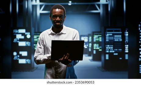 Portrait of smiling admin using laptop to assess energy consumption across server rackmounts components. Professional making sure data center mainframes temperature sensors are running smoothly