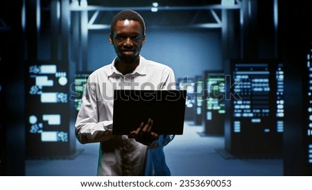 Portrait of smiling admin using laptop to assess energy consumption across server rackmounts components. Professional making sure data center mainframes temperature sensors are running smoothly