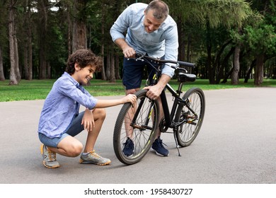 Portrait of smiling adult father and son checking tire of their bicycle after repair, touching wheel, standing on the road at public park, spending time together outdoors in the summer - Powered by Shutterstock