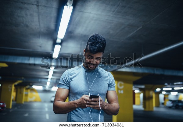 Portrait of a smiling african\
american athlete man listening to music in the underground car\
parking.