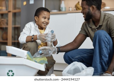 Portrait of smiling African American boy sorting plastic for recycling at home with father - Powered by Shutterstock