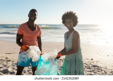 Portrait of smiling african american couple cleaning beach from plastic waste on sunny day. unaltered, togetherness, responsibility and environmental issues concept. - Powered by Shutterstock