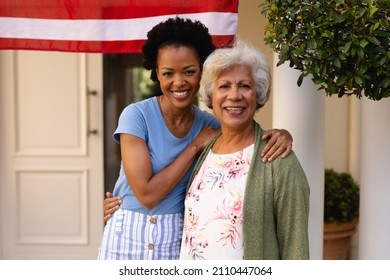 Portrait of smiling african american daughter with arm around mother at house entrance. family and bonding, unaltered.