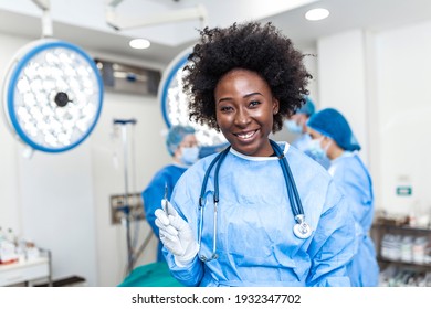 Portrait Of Smiling African American Female Surgeon In Surgical Uniform Holding Scalpel At Operating Room. Young Woman Doctor In Hospital Operation Theater
