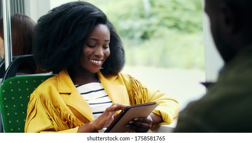 Portrait of smiling african american girl with an afro hairstyle  using tablet in public transport. 