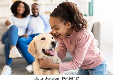 Portrait of smiling African American girl whispering something in the ear to her pet, telling secret and emracing happy dog, spending time together with best friend in living room, selective focus