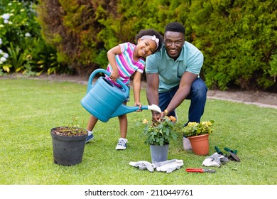 Portrait of smiling african american girl watering plants by father kneeling in garden. family, love and togetherness concept, unaltered. - Powered by Shutterstock