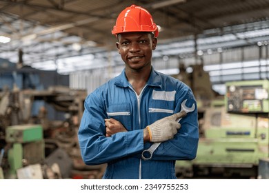 Portrait of smiling African American industrial worker man with helmet crossed arms holding wrench industry factory .happy confidence black male Engineer standing in manufacturing.