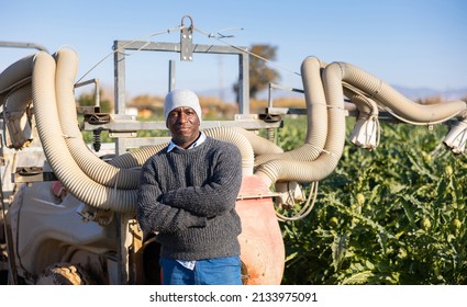 Portrait of smiling african american male farmer standing near tractor with fumigator at the farm field - Powered by Shutterstock