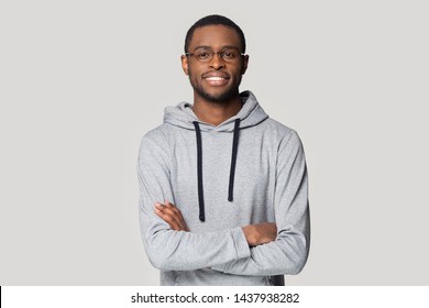 Portrait of smiling african American man in glasses and sportswear isolated on grey studio background pose for picture, happy black male in eyewear and hoodie stand with arms crossed look at camera