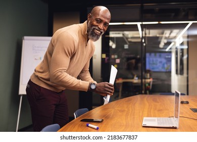 Portrait of smiling african american mature businessman with documents at desk in office. Unaltered, creative business, planning, strategy, positive emotion. - Shutterstock ID 2183677837
