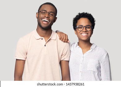 Portrait Of Smiling African American Millennial Couple In Glasses Stand Isolated On Grey Studio Background, Happy Ethnic Black Man And Woman Wear Spectacles Laugh Posing Together For Picture