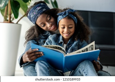 Portrait Of Smiling African American Mother And Daughter Looking At Family Photo Album At Home