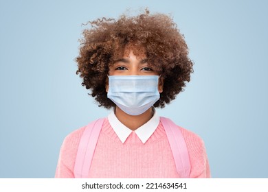 Portrait Of Smiling African American School Girl Or College Student With Curly Afro Hair Wearing Medical Mask, Isolated On Blue Background