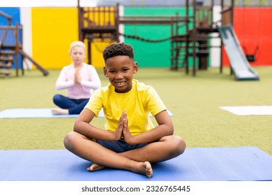 Portrait of smiling african american schoolboy practicing yoga meditation in schoolyard, copy space. Education, inclusivity, elementary school and learning concept. - Powered by Shutterstock