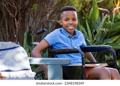 Portrait of smiling african american schoolboy in wheelchair, sitting in garden, with copy space. Education, childhood, inclusivity, elementary school and learning concept. - Powered by Shutterstock