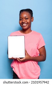 Portrait Of Smiling African American Woman Holding Tablet Computer With White Display Standing In Studio With Blue Background. Teenager Recommending Advertisement Ipad Application. Isolated Touchpad