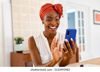 Portrait of smiling african american woman waving hand while on video call using smartphone. Happy black woman in conversation using cellphone at home and wearing traditional turban. Video conference  - Shutterstock ID 2132995983