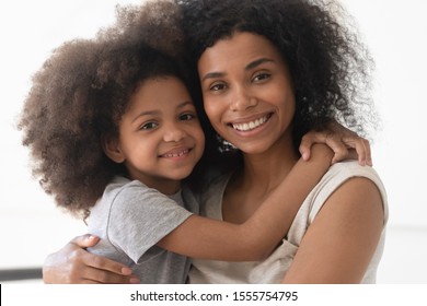 Portrait Of Smiling African American Young Mom Hold In Arms Hug Cute Little Mixed Race Daughter Posing For Picture Together, Happy Biracial Mother Cuddle Embrace Small Girl Child Looking At Camera