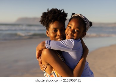 Portrait Of Smiling African American Young Woman With Short Hair Embracing Daughter Against Sea. Sunset, Nature, Unaltered, Beach, Childhood, Family, Togetherness, Lifestyle, Enjoyment And Holiday.