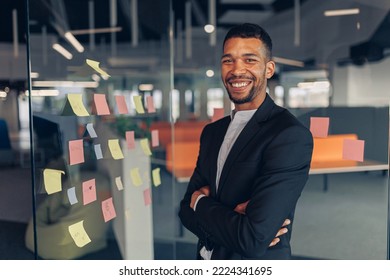 Portrait of smiling african businessman standing in office with crossing hands - Shutterstock ID 2224341695