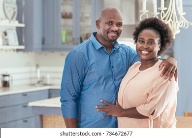 Portrait Of A Smiling African Couple Affectionately Standing Together In Their Kitchen At Home