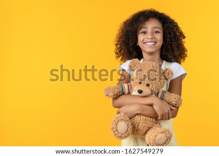 Portrait of smiling african girl hugging teddy bear toy isolated on yellow background