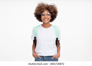 Portrait of smiling african school girl wearing white t-shirt, glasses and backpack, isolated on gray background