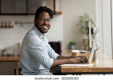 Portrait of smiling African young businessman with dreadlocks sit at workplace home office room working on laptop. Happy successful millennial hipster guy do freelance telework, smile look at camera - Powered by Shutterstock