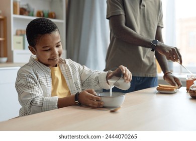 Portrait of smiling African-American boy pouring glass of milk into cereal bowl at breakfast copy space - Powered by Shutterstock