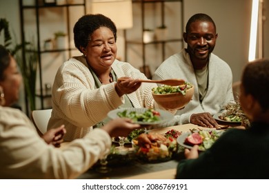 Portrait Of Smiling African-American Grandmother Serving Food While Celebrating Thanksgiving With Big Happy Family At Dinner Table